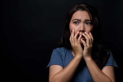 Scared young woman looking away while standing against black background