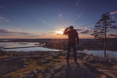 Rear view of man standing on rock against sky during sunset