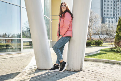 Happy young girl in glasses wearing a pink jacket and jeans