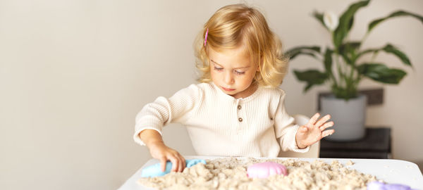 Cute happy caucasian,blonde,curly-haired toddler,baby girl playing with kinetic sand indoors