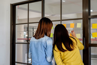 Rear view of woman with colleague writing on adhesive note at office