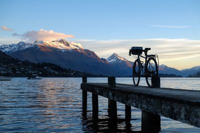Bicycle on pier over lake by mountains against sky during winter