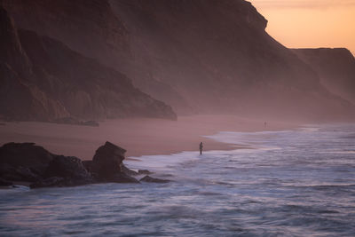 Scenic view of sea by mountain during sunset