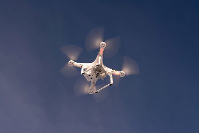 Low angle view of drone flying against sky on sunny day