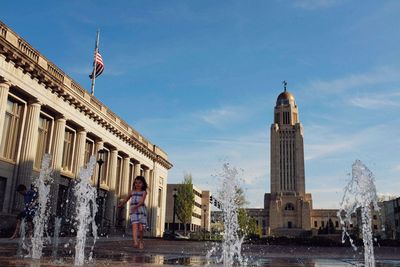 Girl walking at fountain in city against sky