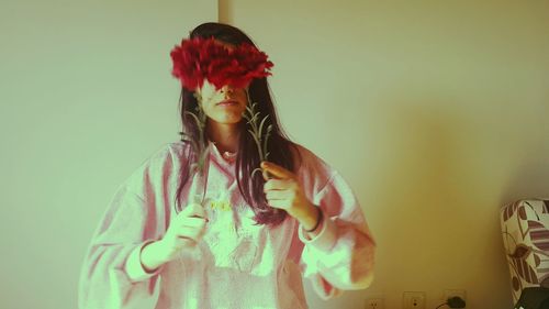 Young woman with long hair holding flowers against wall at home