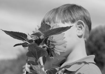 Close-up of boy with sunflower against sky