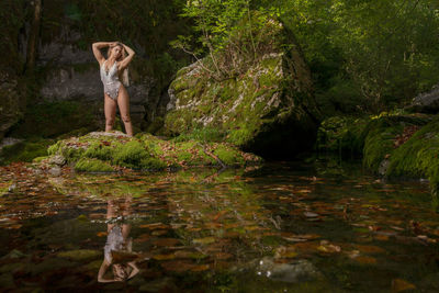 Young woman in lingerie standing by lake in forest