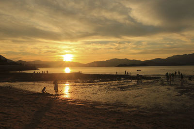 Silhouette people on beach against sky during sunset