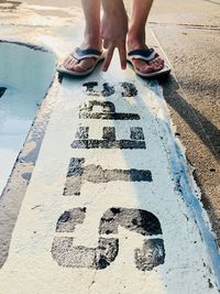 Low section of man showing peace sign text at footpath