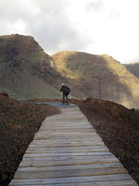 Rear view of man walking on footpath leading towards mountain against sky