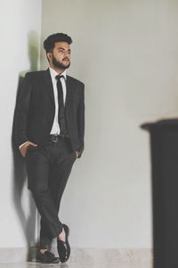 Full length of handsome young man with hands in pockets standing against wall at home