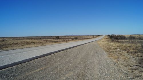 Road amidst land against clear blue sky