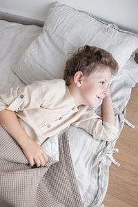 Boy in home clothes joyfully lies in natural bedding after waking up.