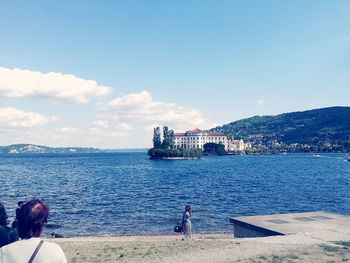 Rear view of people on sea by city against sky