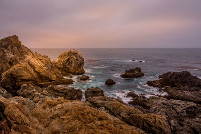 Rocks on beach against sky during sunset