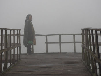 Man standing on railing against sky