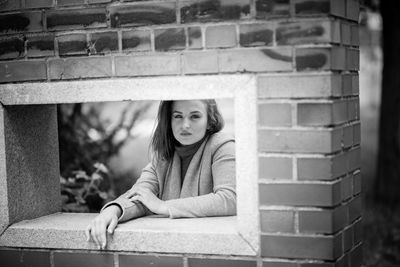 Portrait of woman sitting against brick wall
