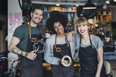 Portrait of happy multi-ethnic mechanics with gears in workshop