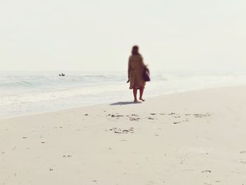 Rear view of man walking on beach against clear sky