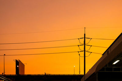 Low angle view of power lines against orange sky