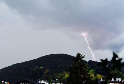 Low angle view of lightning over trees against storm clouds