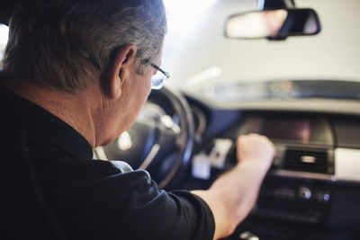 Close-up of senior mechanic examining air conditioner while sitting in car