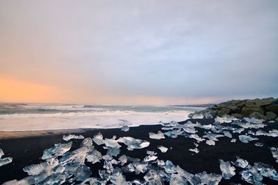 Icebergs at beach against sky during sunset