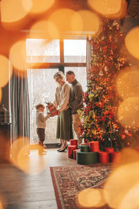 Portrait of happy family in knitted beige sweaters waiting santa indoor.