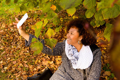 Smiling woman taking selfie on leaves covered field at autumn