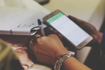 Cropped hand of woman using mobile phone while writing