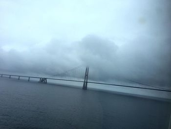 Suspension bridge over sea against cloudy sky