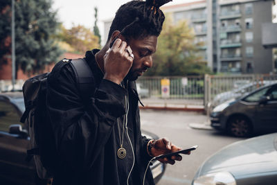 Man adjusting in-ear headphones while using mobile phone