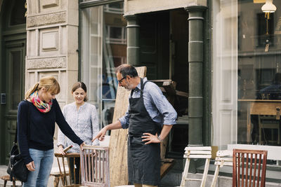 Smiling retailers assisting woman outside shop