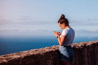 Side view of woman sitting on rock by sea against sky