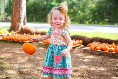 Portrait of happy girl standing by pumpkins on field