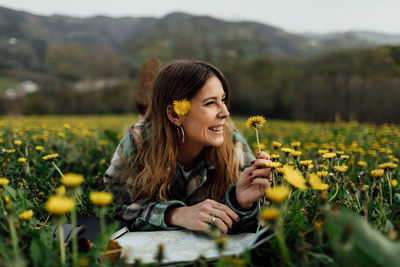 Smiling young woman with yellow flower in field