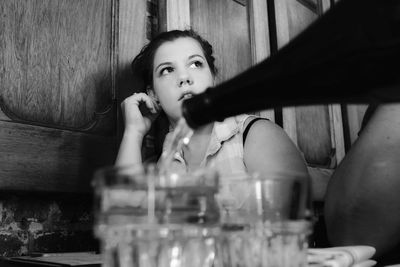 Close-up of bottle pouring drink in glass against young woman at restaurant