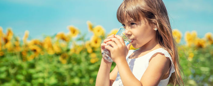 Young woman drinking water while standing amidst plants