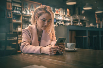 Young woman using smartphone in cafe with dark lighting.