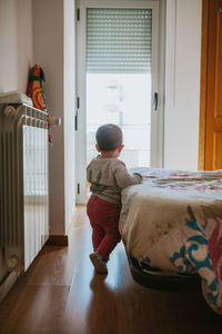 Full length of baby girl standing by bed at home