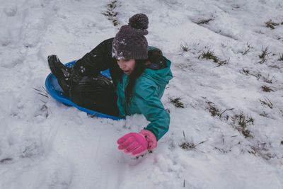 Full length of girl sitting on bobsled in snow