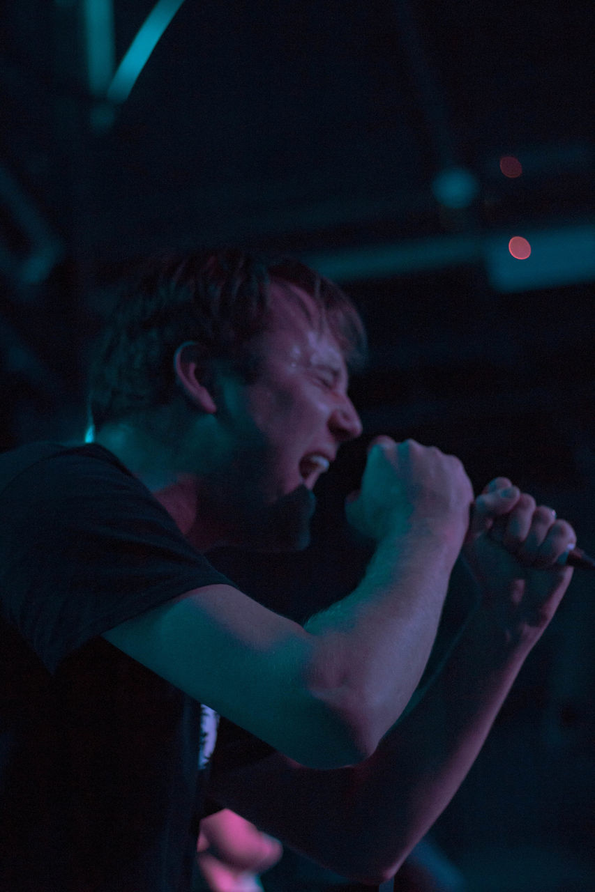 SIDE VIEW OF YOUNG MAN LOOKING AWAY WHILE STANDING IN NIGHTCLUB