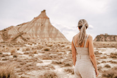 Rear view of woman standing on field against rock mountain