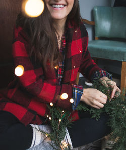 Midsection of woman making wreath while sitting at home during christmas