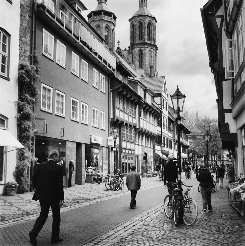 building exterior, architecture, built structure, street, walking, city, person, men, city life, large group of people, lifestyles, city street, sky, cobblestone, full length, leisure activity, building, sidewalk, street light