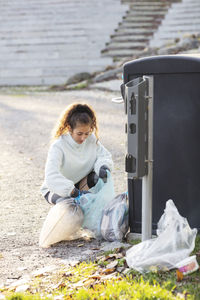 Female volunteer crouching with plastic waste by garbage can