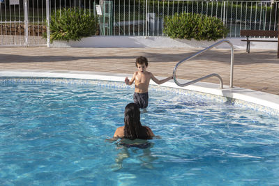 Mother and young son enjoying a swim in a residential pool, with the boy holding onto the ladder.