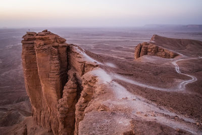 Distant view of woman standing at cliff against landscape