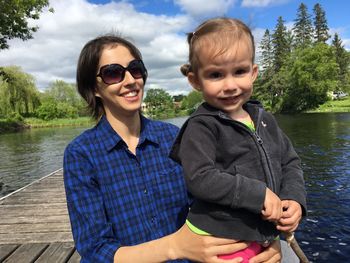 Mother holding daughter while standing on pier against sky